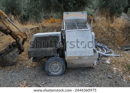 A Stone Mortar Mixer construction machine stands on a construction site in Lardos Village. A concrete mixer, cement mixer is a device that homogeneously combines cement, aggregate, and water.