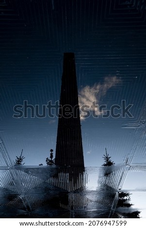 Stone obelisk of the monument to the Heroic Defenders of Leningrad in the reflection of a puddle.