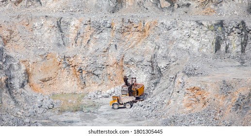 Stone Open Pit Mine. Excavator Is Loading Raw Materials Into Yellow Truck For Transport To Combine.