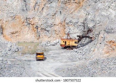 Stone Open Pit Mine. Excavator Is Loading Raw Materials Into Yellow Truck For Transport To Combine.