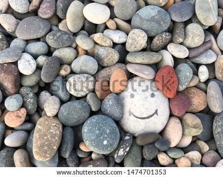 Stone with a painted smile. On the shore, one stone stands out from the others. On a small stone is an image of a happy face. Concept: joy, happiness, positive, kindness.