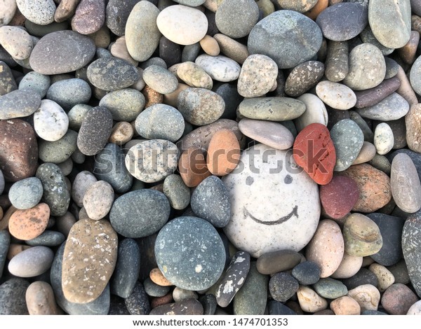 Stone with a painted smile. On the shore, one stone stands out from the others. On a small stone is an image of a happy face. Concept: joy, happiness, positive, kindness.