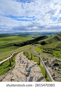Stone path leading down through green hills with wooden railings under cloudy sky