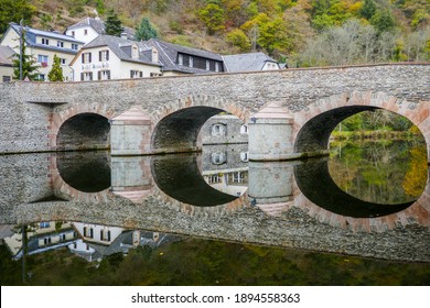 Stone Pedestrian Bridge With Arches Reflecting In The Water Of The Sûre River. Shot In The Picturesque Village Of Esch-sur-Sûre In Luxembourg.