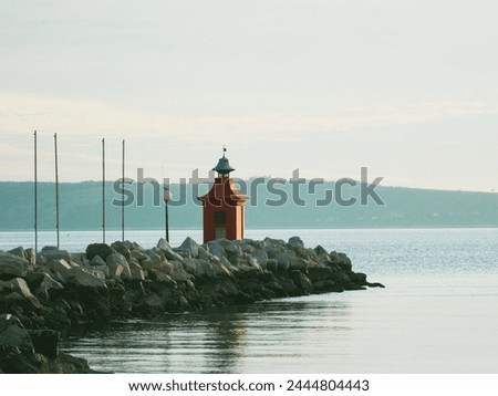 A stone pier made of large rocks and surrounded by the sea with a red lighthouse