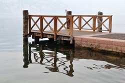 Stone Pier And Timber Jetty On Misty Waters Of Italian Lake Garda 