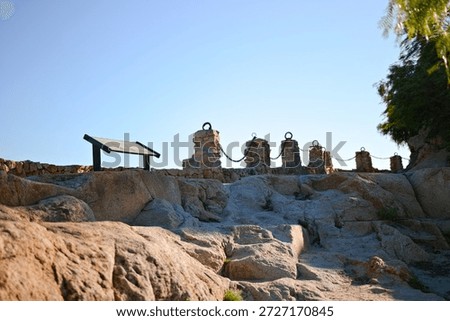 Stone posts connected by metal chains line a rocky hillside overlook at Mount Rubidoux in Riverside, California beneath clear blue skies.