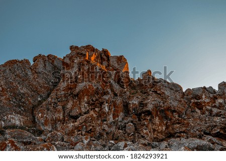 Stone rock in red textured moss in orange bright light of sunset. Cliff illuminated by sun on clear sky background. Baikal nature