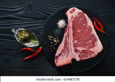 Stone slate tray with raw black angus club steak and condiments, top view over black wooden surface - Powered by Shutterstock