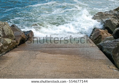 Stone slipway with blue ocean, sea breaking waves and rocks