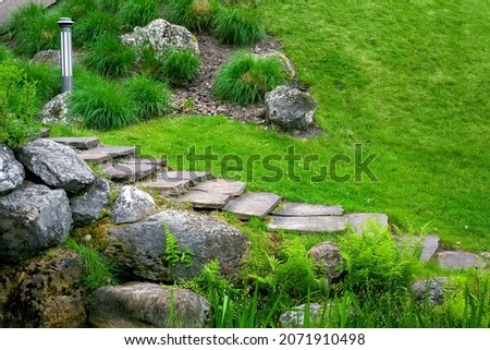 stone staircase with steps made of wild natural stone on slope of hill park landscape with rock, ground garden lantern among green plants in summer environment for eco travel, nobody.