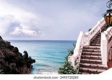 Stone staircase with white railings leading to a stunning view of the Mediterranean Sea on a cloudy day. - Powered by Shutterstock