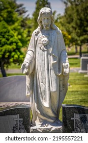 Stone Statue Of Jesus Christ Holding Out His Hands Mounted On The Top Of A Cemetery Headstone