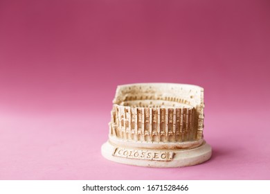 Stone Statuette Of The Coliseum Building In Rome In Italy. Concept Of Dangerous Infection With The Chinese Coronavirus Covid-2019. Pink Background. Beautiful Memory Souvenir For Travelling Tourists.