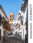 Stone street between white houses with church tower in the background in Zafra with tower of Iglesia de la Candelaria, Badajoz, Spain. Rural tourism concept.