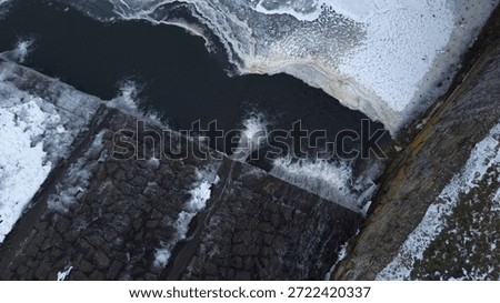A stone structure displays ice formations. Water cascades over a ledge. Snow covers surfaces. The scene exhibits a wintry atmosphere. Dark water fills a basin - Plzen, Czech - Jan,6,2026