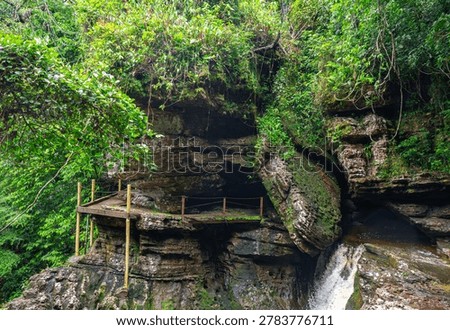A stone structure with a viewing platform overlooks a serene waterfall, framed by vibrant green foliage in Colombia's rich landscape.