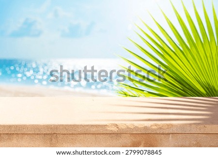 Stone table for placing product overlooking blurred seascape with tropical beach landscape and green palm leaves