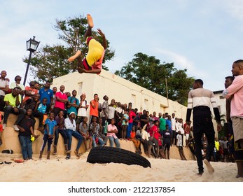 Stone Town, Zanzibar, Tanzania - January 2021: Crowds of people watch like young people jump on an inner tube on a sandy beach in Stone Town. Africa