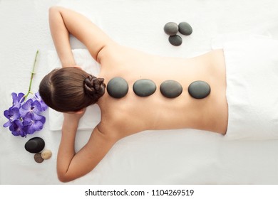 Stone treatment. Top view of beautiful young woman lying on front with spa stones on her back.  Beauty treatment concept.