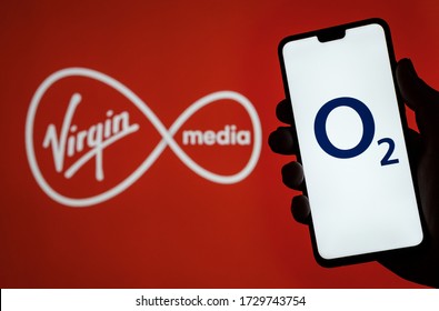 Stone  UK - May 12 2020: O2 Telefonica Logo On Smartphone Screen Hold In Hand And Virgin Media Logo On Blurred Background. Concept For Virgin And O2 Merger.