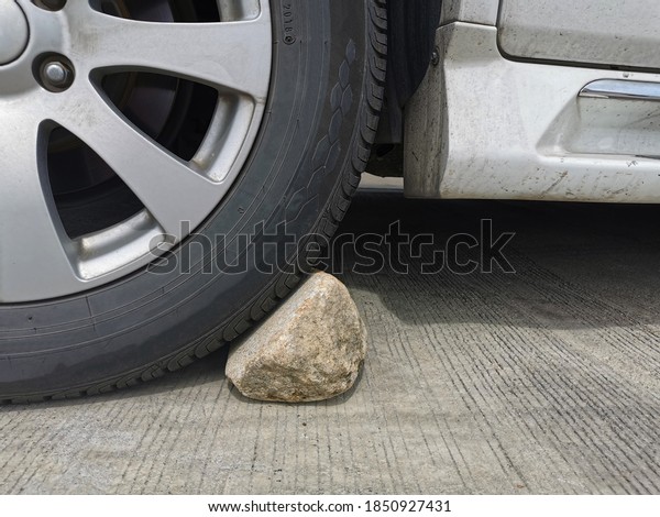 Stone under the wheel of the car to prevent car\
rolling. Vehicle’s wheels chock. parking on the mountain or hill.\
Safety concept.