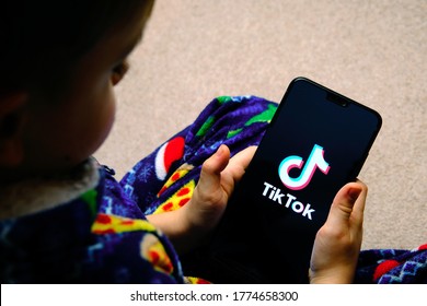 Stone / United Kingdom - July 12 2020: TikTok App Logo On A Smartphone Screen And Young Child Holding It In His Hands. Concept For TikTok And Child Privacy.