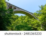 The stone Vintgar Gorge Viaduct in Slovenia showcased in a low-angle view, revealing its historic arch and stone construction, framed by lush green trees in the Julian Alps.