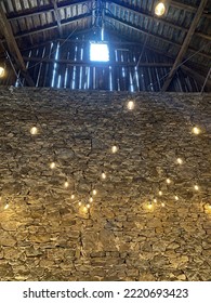 Stone Wall In A Barn With Fairy Lights Draped Among The Rafters And An Open Window