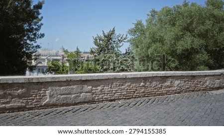 Stone wall and cobblestone foreground in sharp focus with defocused city buildings and trees in soft bokeh; background backplate copyspace calm.