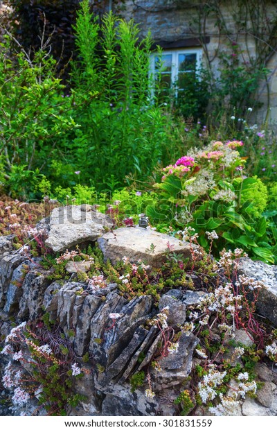 Stone Wall In Front Of An Overgrown Cottage Garden In Bibury
