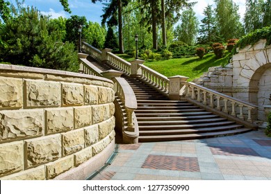 stone wall near the marble staircase with balustrades and iron lanterns against a landscape with green plants in the park garden of the mansion.
