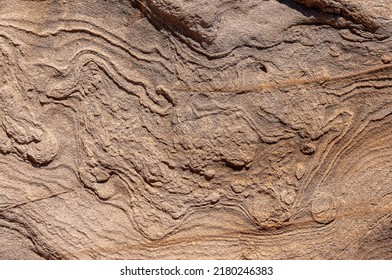 Stone wall is sand colored with various patterns and spots. Textured stone background of sand color with wavy patterns.