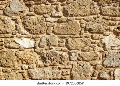 Stone Wall Texture Background, Exterior Of Ancient Greek House In Paphos Archaeological Park, Cyprus. Abstract Pattern Of Old Building Wall Close-up, Rough Yellow Surface For Backdrop Or Wallpaper. 