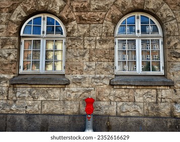 Stone wall with two white window and red hydrant equipment in the middle