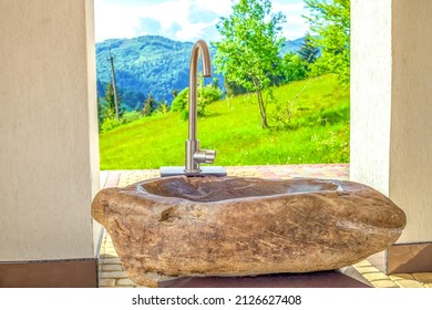 Stone washbasin in spring sunny yard. Modern sink in summer backyard at sun light day. Rural landscape with natural rock washstand by mountain background, front view
