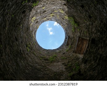 Stone well hole, old construction from inside, brick walls and blue sky background, fall down in the well concept - Shutterstock ID 2312387819