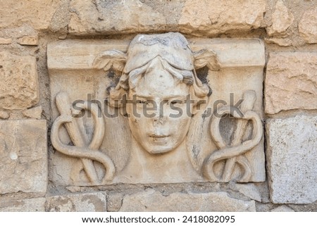 Stone-carved head of Hermes with wings rising from his hair and caduceus on both sides on the ruins of an ancient Roman time wall in Spain
