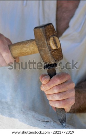 A stonemason uses a hammer and chisel to work on the stone at the Guédelon medieval castle construction site. Treigny, France.