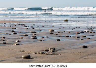 Stones dot Swami's Beach in Encinitas, California, with a lone surfer in the background.  - Powered by Shutterstock