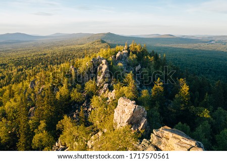 Stones of rocky Ural-Tau ridge among green forest at sunset, panoramic aerial view. Ural mountains wild nature landscape near Zlatoust, Chelyabinsk Oblast, Russia