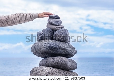 Stones tower on the coast of the sea in the nature. Ocean beach, nine pebbles tower. Female hand put the last piece. Concept of balance and harmony.