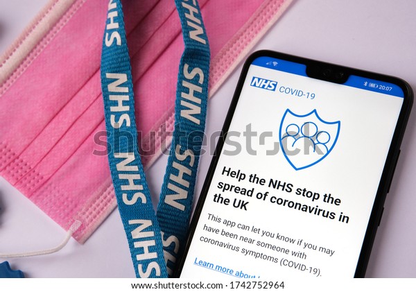 Stone/UK - May 27 2020:\
NHS COVID-19 contract tracing app start screen seen on the mobile\
device which is placed next to blue NHS lanyard and pink face mask.\
Selective focus. 