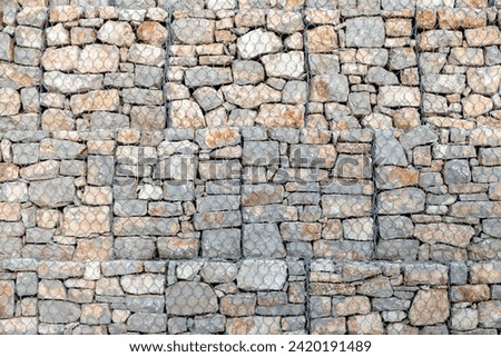 Stonewall behind wire mesh background texture. Metal lattice for protection in front of empty grey rocky wall construction backdrop. Copy space
