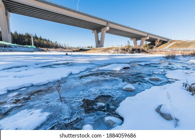 Stoney Trail construction and highway bridge over snowy frozen creek landscape. City transportation and engineering. Bridge built over beautiful running stream at winter 