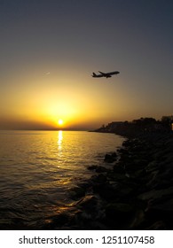 Stony Coast And Sea At Evening With Airplane Silhoutte And Sun