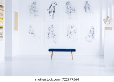 Stool On White Floor Against Wall With Drawings In Bright Art Gallery With Sculpture