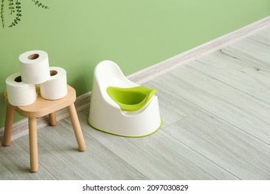 Stool with toilet paper rolls and white potty on grey wooden floor near color wall