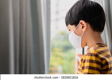 Stop Asian Hate And Covid 19 Pandemic Fatigue Concept. A Little Asian Boy Wear Medical Face Mask, Look Out The Window. Social Distancing. Quarantine, Isolated, Infected, Coronavirus Disease, Lockdown.