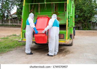 Stop Biohazard,Garbage Men In Coronavirus Hazmats Working Together On Emptying Dustbins For Trash Removal With Truck Loading Waste And Trash Bin.